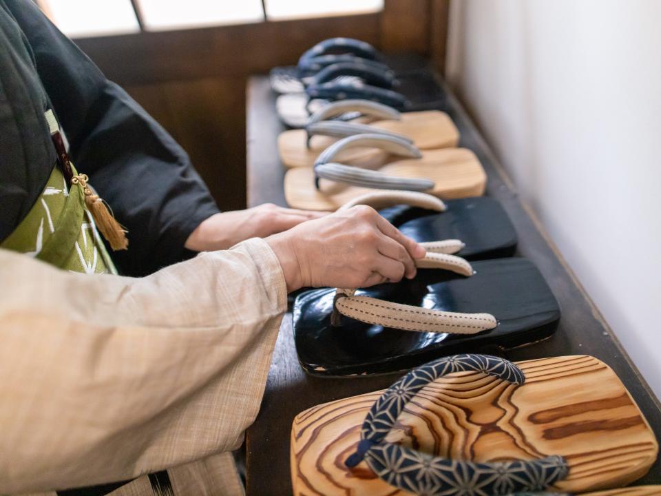 A person picks up a pair of wooden sandals from a neatly-organised selection.