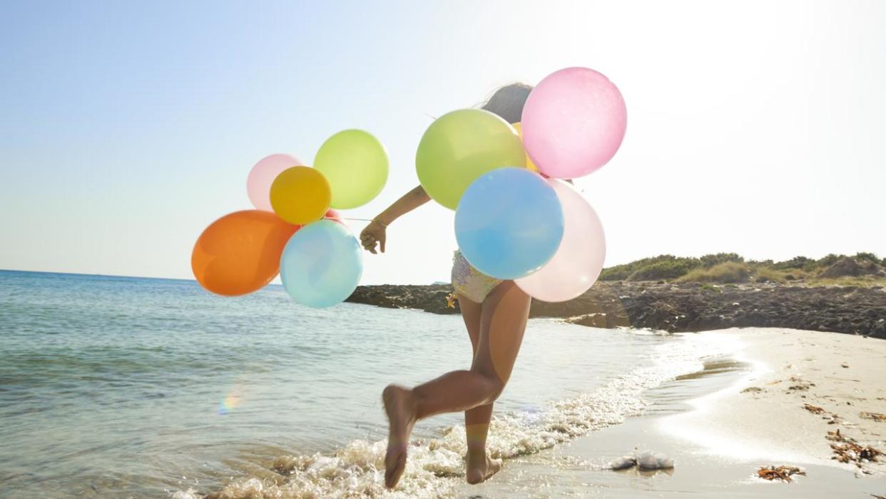 Little girl running with balloons on the beach
