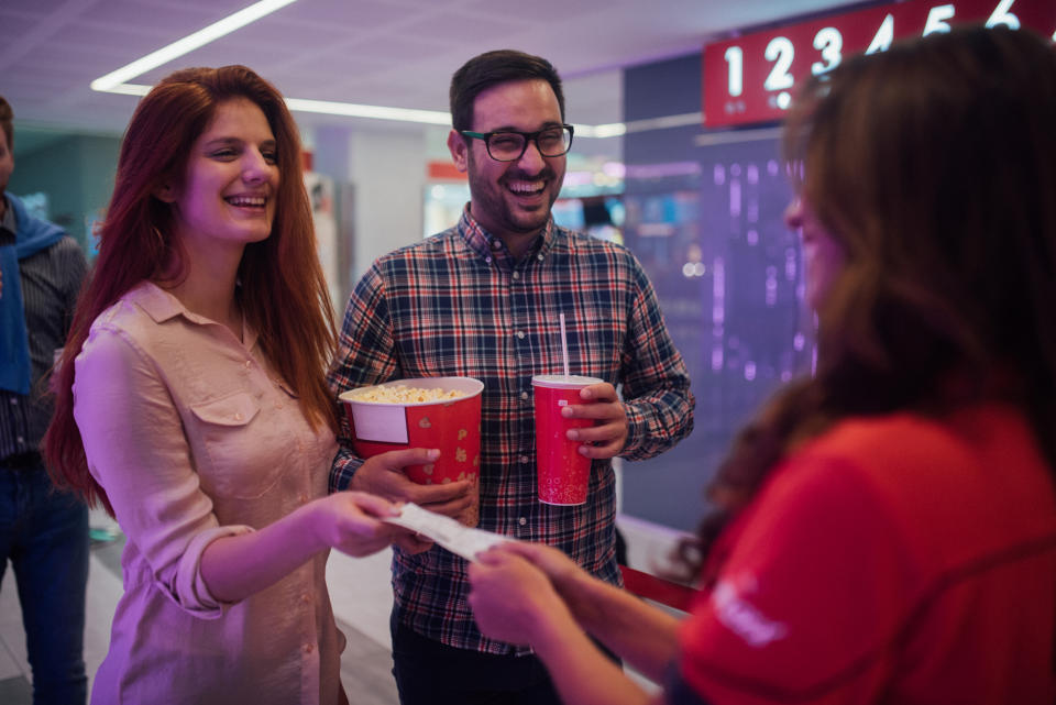 Two people receiving movie tickets from an attendant at a cinema counter