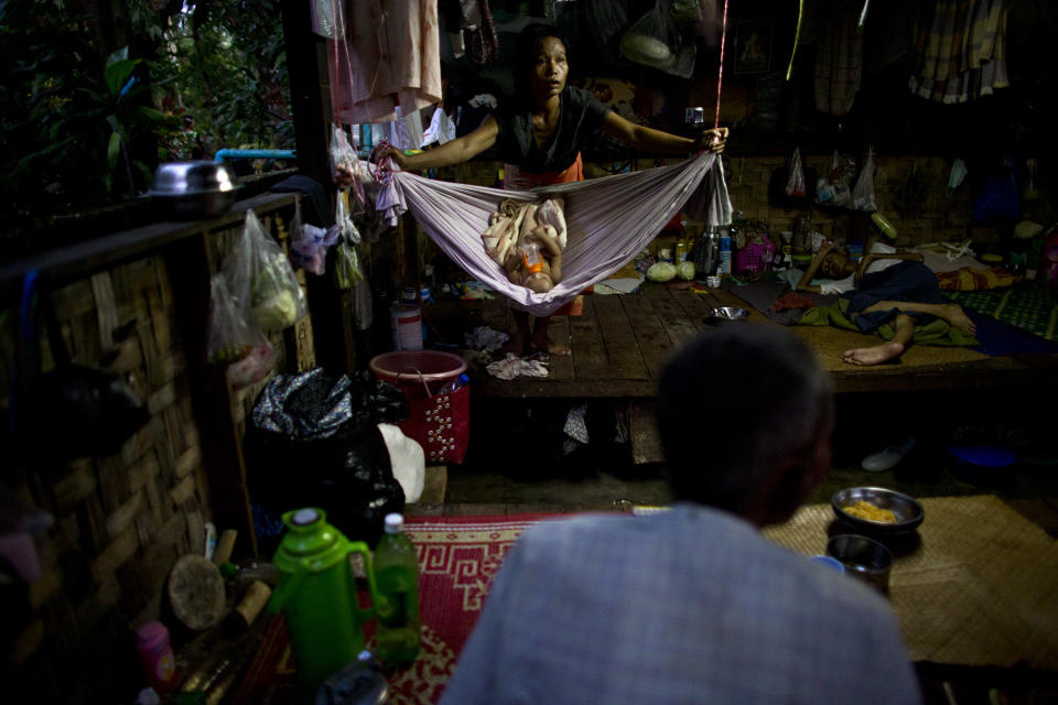 In this Aug. 29, 2012 photo, HIV-infected mother Maw, 36, center, sways a hammock for her 5-month-old daughter Ei Ei Phyu, also infected with HIV, who is sucking a milk bottle, inside a hut shared with other HIV-infected patients at an HIV/AIDS center on the outskirts of Yangon, Myanmar. Following a half century of military rule, care for HIV/AIDS patients in Myanmar lags behind other countries. Half of the estimated 240,000 people living with the disease are going without treatment and 18,000 are dying from it every year.(AP Photo/Alexander F. Yuan)