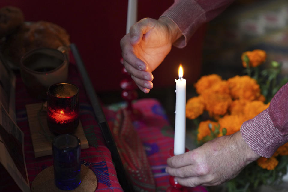 Sebastian Diaz Aguirre steadies a candle in an altar dedicated to his father, who died in a nursing home in Mexico last month, for Day of the Dead in his home in the Brooklyn borough of New York, Wednesday, Oct. 28, 2020. "He didn't die of COVID, but me and my brother said the same exact thing, that it was the pandemic that killed him," said Diaz Aguirre. (AP Photo/Emily Leshner)