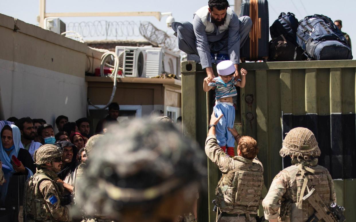 An Afghan man hands his child to a British paratrooper during the airlift from Kabul  - AP