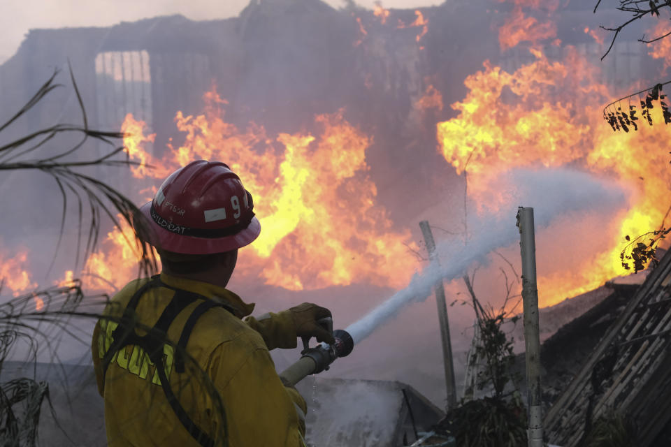 A firefighter tries to extinguish the flames at a burning house as the South Fire burns in Lytle Creek, San Bernardino County, north of Rialto, Calif., Wednesday, Aug. 25, 2021. (AP Photo/Ringo H.W. Chiu)