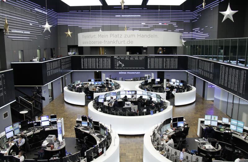 Traders are pictured at their desks in front of the DAX board at the Frankfurt stock exchange