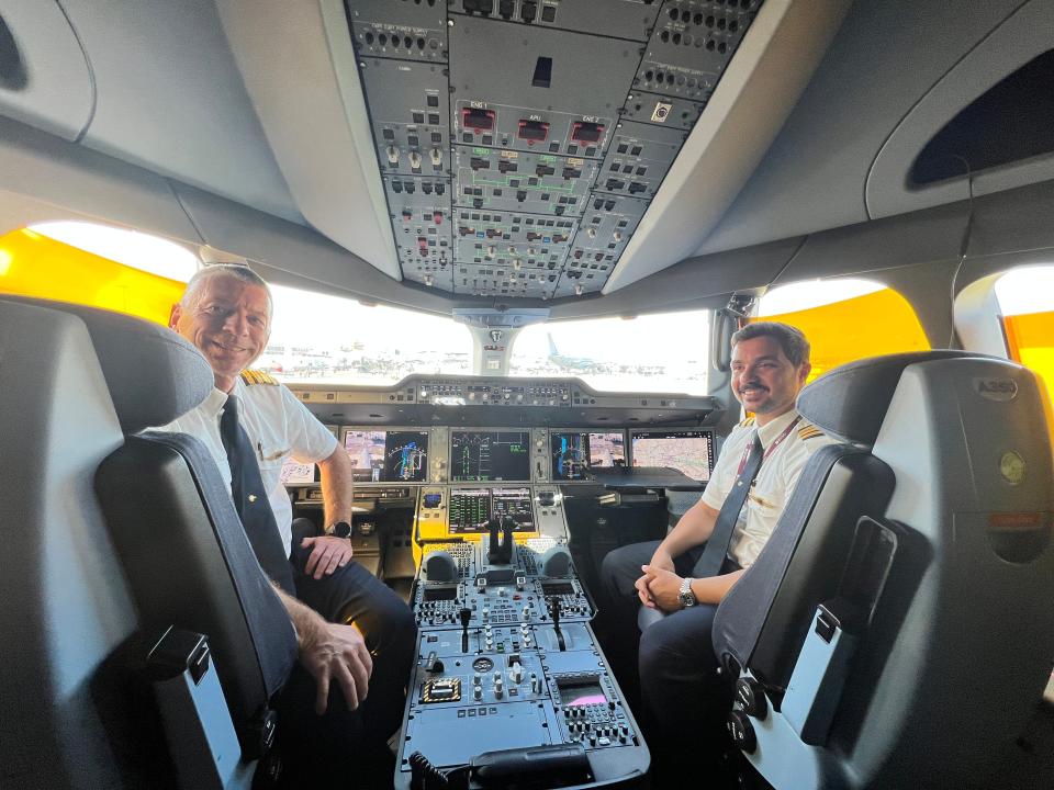 Two Qatar Airways pilots sit and smile for the camera inside the cockpit of an Airbus A350