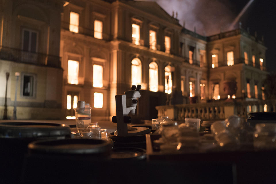 Salvaged equipment lies on the ground as flames engulf the 200-year-old National Museum of Brazil, in Rio de Janeiro, Sunday, Sept. 2, 2018. According to its website, the museum has thousands of items related to the history of Brazil and other countries. The museum is part of the Federal University of Rio de Janeiro. (AP Photo/Leo Correa)