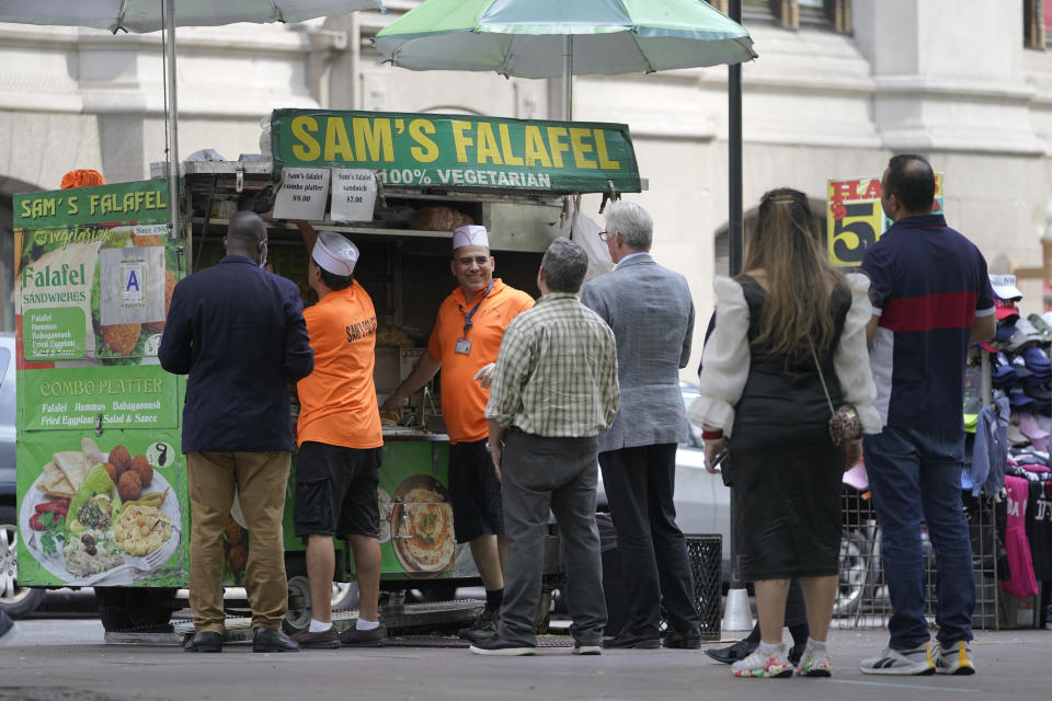 Emad Ahmed, center facing camera, works at his falafel cart in Zuccotti park in the financial district of New York, Tuesday, Sept. 13, 2022. It's becoming clearer that New York City's recovery from the pandemic will be drawn out and that some aspects of the city's economic ecosystem could be changed for good. More workers returned to their offices as the summer ended. But those limited numbers mean continued hardship for New Yorkers whose jobs are built around the commuting class. (AP Photo/Mary Altaffer)