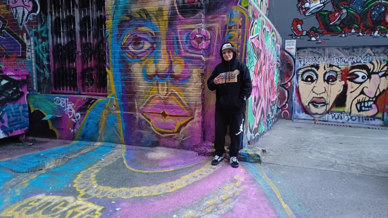 Street artist James Hardy, a.k.a. Smokey D, poses in front of murals in the city's first legal graffiti wall near Pender Street in Vancouver. The artist is due to be a guest lecturer at Emily Carr University this spring. (Akshay Kulkarni/CBC - image credit)