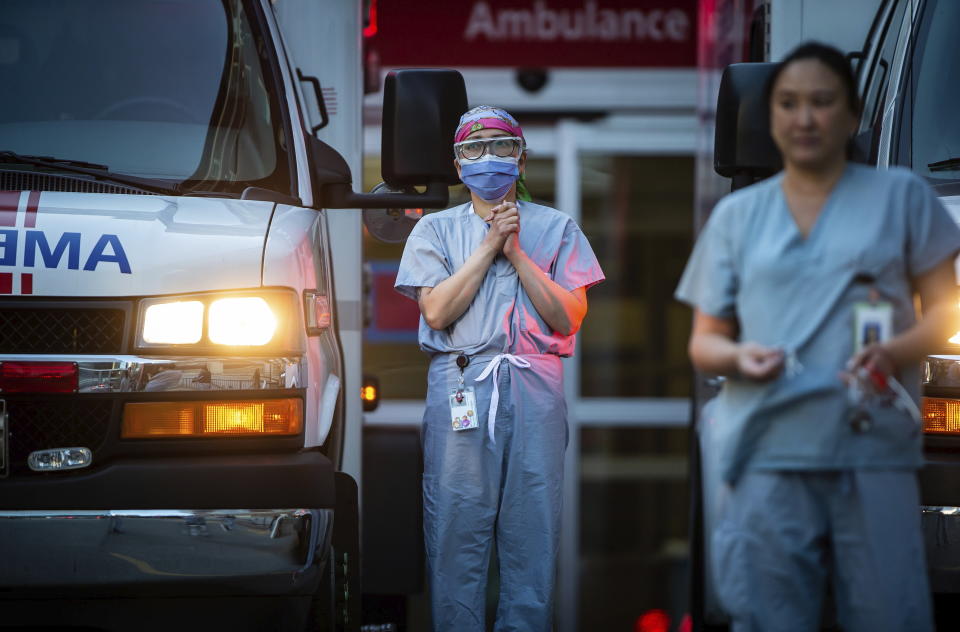 Healthcare workers at St. Paul's Hospital acknowledge applause and cheers from people outside the hospital, as a convoy of first responders with lights and sirens activated parade past to show support for the hospital staff, in Vancouver, British Columbia, April 5, 2020. (Darryl Dyck/The Canadian Press via AP)