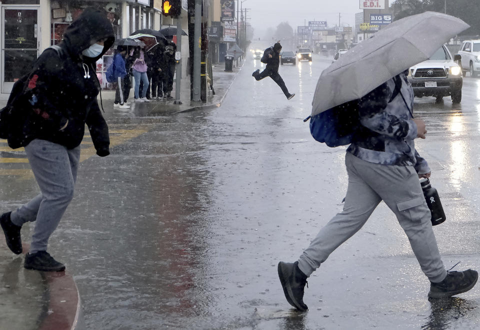 Students cross Topanga Canyon Blvd. early Friday morning, Feb. 24, 2023, as they make their way to Canoga Park Senior High School in the pouring rain. (Dean Musgrove/The Orange County Register via AP)