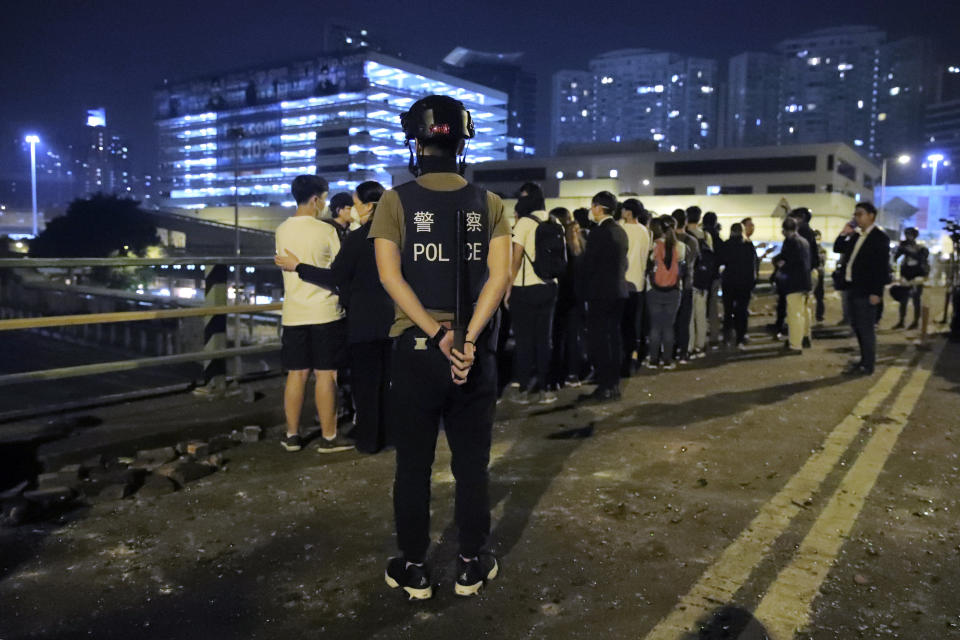 A riot policeman watches over a group of detained people on a bridge in Hong Kong, early Tuesday, Nov. 19, 2019. About 100 anti-government protesters remained holed up at a Hong Kong university Tuesday as a police siege of the campus entered its third day. (AP Photo/Kin Cheung)