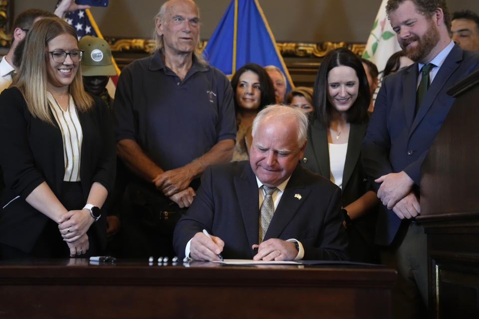 Minnesota Gov. Tim Walz, middle, signs a bill to legalize recreational marijuana for people over the age of 21, making Minnesota the 23rd state to do so, Tuesday, May 30, 2023, in St. Paul, Minn. Former Minnesota Gov. Jesse Ventura stands in background second from left. (AP Photo/Abbie Parr)