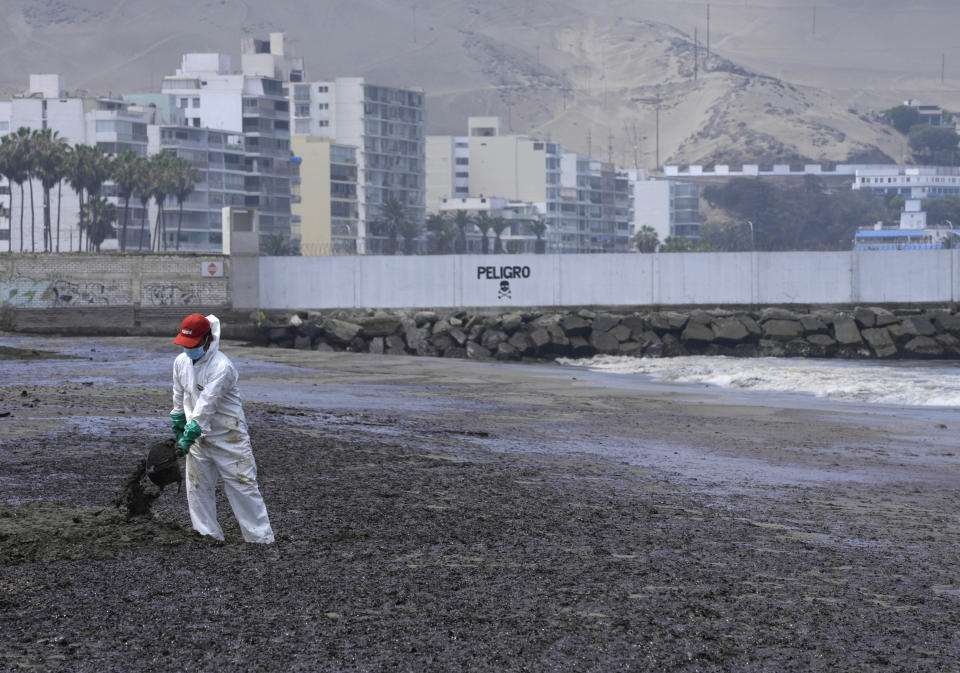 A worker, dressed in protective suit, cleans Conchitas Beach contaminated by an oil spill, in Ancon, Peru, Thursday, Jan. 20, 2022. The oil spill on the Peruvian coast caused by the waves from an eruption of an undersea volcano in the South Pacific nation of Tonga has expanded along the coastline, reaching Ancon, a fishing and touristic port. (AP Photo/Martin Mejia)
