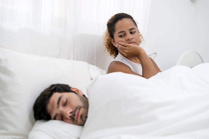 a couple in bed where the man is sleeping and the woman is nervously looking at him