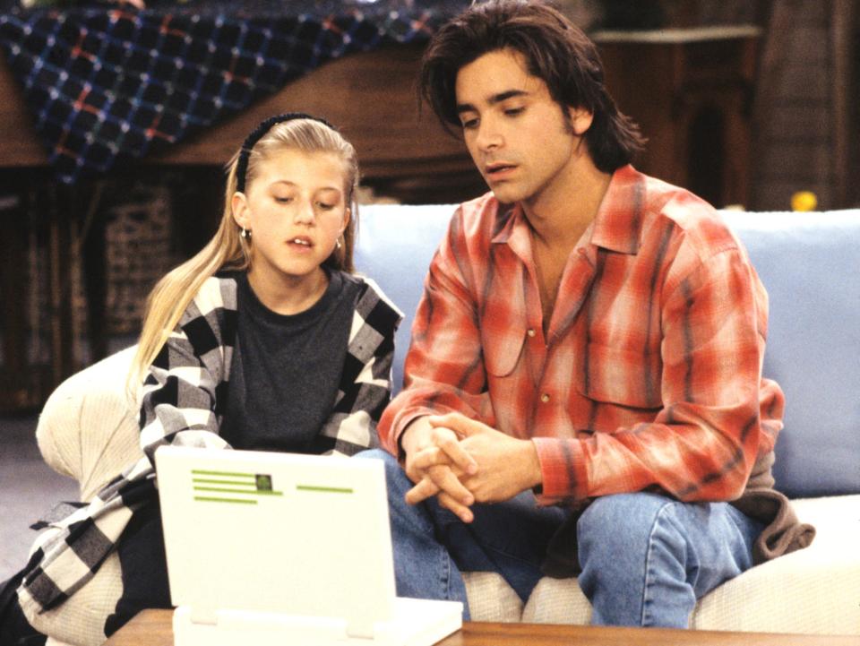 Jodie Sweetin and John Stamos sitting on a couch