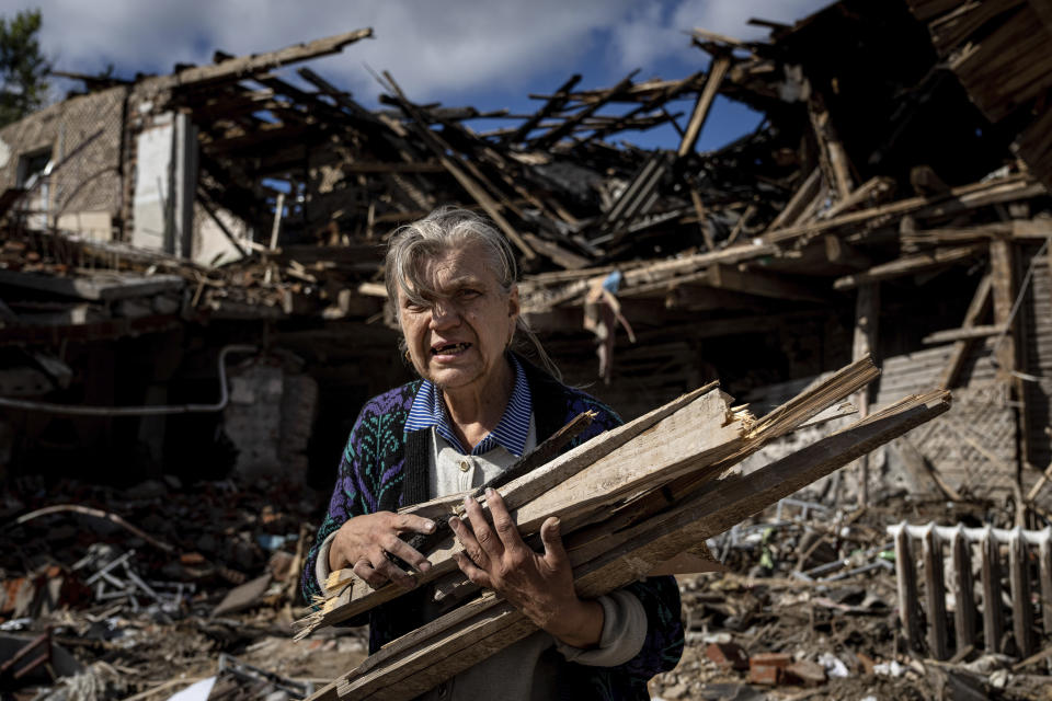 FILE - A woman collects wood for heating from a destroyed school where Russian forces were based in the recently retaken area of Izium, Ukraine, Monday, Sept. 19, 2022. As milestones go, the first anniversary of Russia's invasion of Ukraine is both grim and vexing. It marks a full year of killing, destruction, loss and pain felt even beyond the borders of Russia and Ukraine. (AP Photo/Evgeniy Maloletka, File)