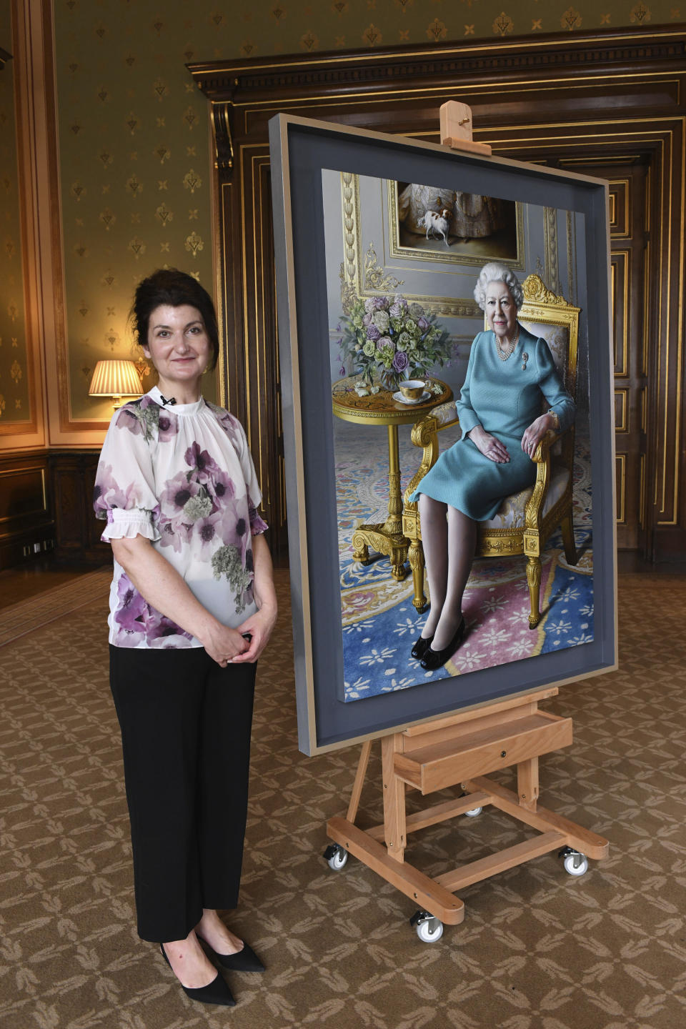 Undated handout photo released Saturday July 25, 2020, by the Royal Communications, showing artist Miriam Escofet after unveiling her painting of Britain's Queen Elizabeth II. The painting was commissioned by the Foreign and Commonwealth Office (FCO), as a 'lasting tribute to her service' to diplomacy. The Queen paid a virtual visit to the FCO via video call, to hear about their response to the COVID-19 outbreak and join the official unveiling of the new portrait painting. (Foreign and Commonwealth Office via AP)