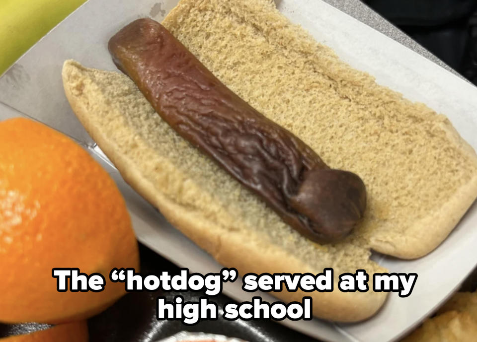 A hot dog with a bun, blurred orange item on the left