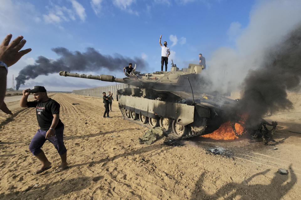 Palästinenser feiern an einem zerstörten israelischen Panzer am Zaun des Gazastreifens (Bild: Hassan Eslaiah/AP/dpa)