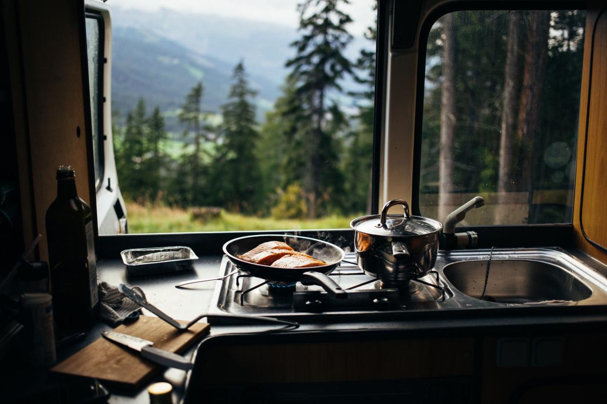 Close up on frying pan with organic salmon prepared in inside camper van on campsite in mountains or forest. Life on the road, camper van lifestyle outdoors vibes. Prepare food in converted vehicle