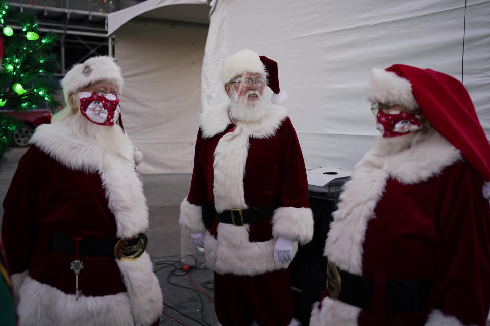 Santa Claus' from left, Larry Hansen, Charlie Bush and Bill Sandeen, wear masks as a precaution against coronavirus while waiting before the opening of a Santa drive-thru selfie station at Glittering Lights, a drive-thru holiday lights display, Thursday, Dec. 10, 2020, in Las Vegas. Santa behind plexiglass. Santa in a life-sized snow globe. Santa wearing a face mask. And, of course, Zoom Santa. In this socially distant holiday season, Santa Claus is still coming to towns (and shopping malls) across America but with a few 2020 rules in effect. (AP Photo/John Locher)