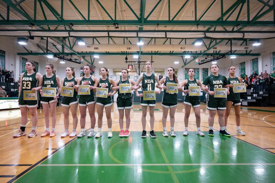 Notre Dame Academy girls' basketball players stand with signs honoring who they play for before a charity game for Ava Blazis, a Sutton native with acute lymphoblastic leukemia, held earlier this month.