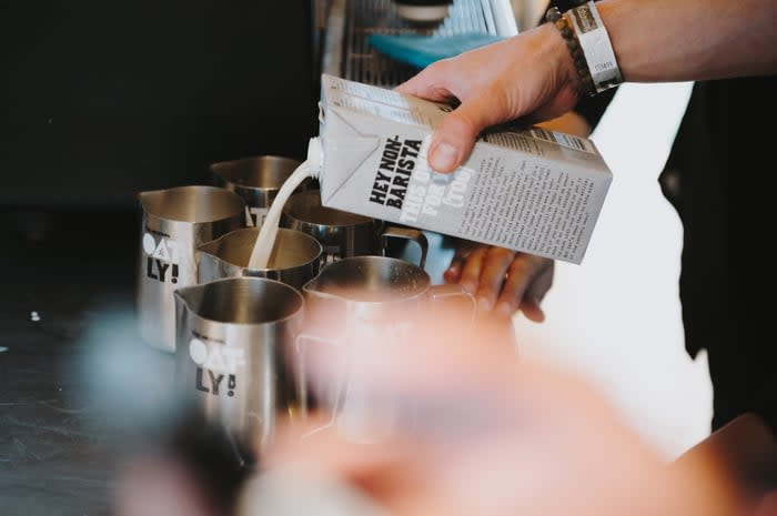 A barista pouring oat milk into a pitcher.