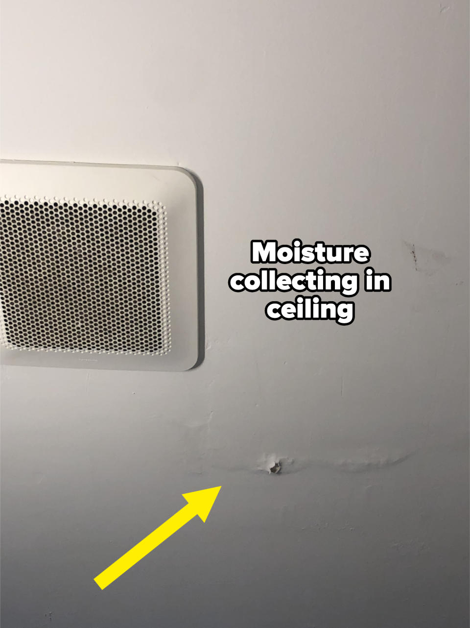 A ceiling with a ventilation cover and a small hole along with some visible water damage