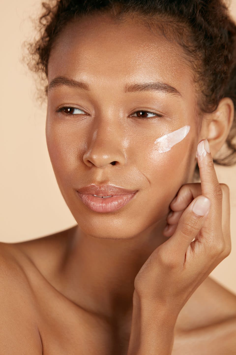 face skin care woman applying cosmetic cream on clean hydrated skin portrait beautiful happy smiling african american girl model with natural makeup applying facial moisturizer, beauty product