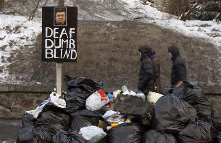 People walk past a sign with a picture of President Viktor Yanukovich at a refuse collection point at the site of clashes with riot police in Kiev, January 27, 2014. REUTERS/Vasily Fedosenko