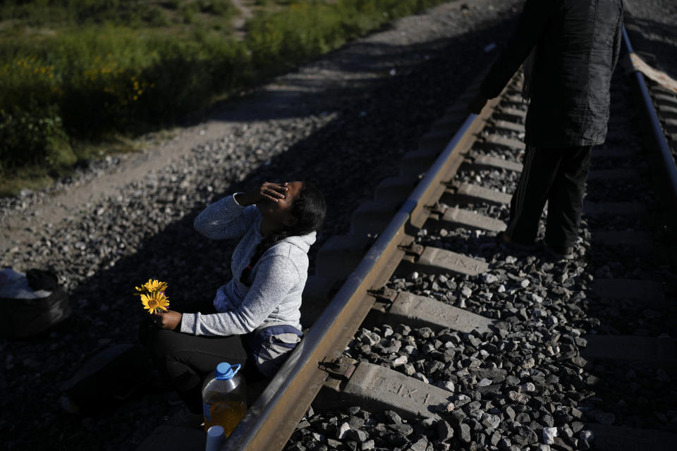 A Venezuelan migrant laughs as she jokes with her husband, who gave her a few flowers he picked in the grass, as they wait along the rail lines in hopes of boarding a freight train heading north in Huehuetoca, Mexico, Wednesday, Sept. 20, 2023. (AP Photo/Eduardo Verdugo)