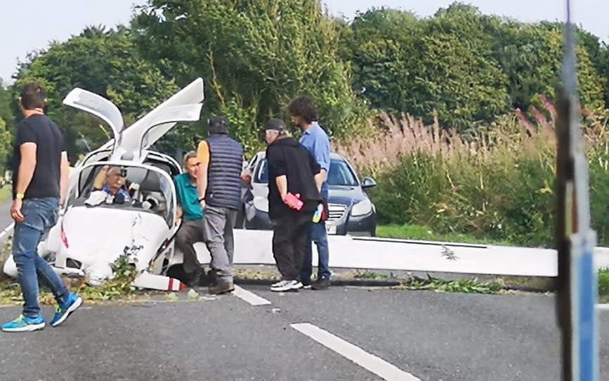 Drivers get out of their cars to help the pilot and passenger out of the aircraft