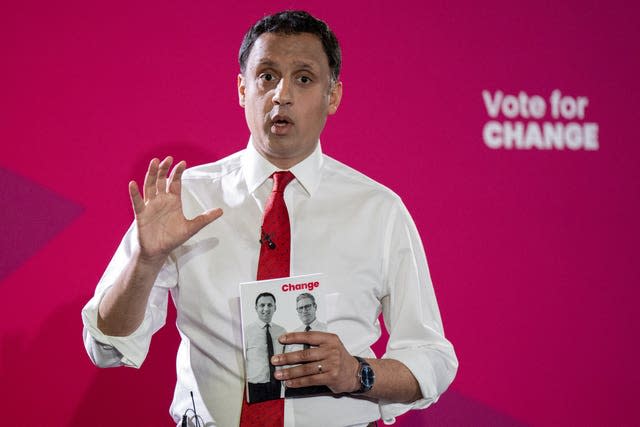 Anas Sarwar holding the Labour manifesto, in front of Labour 'vote for change' signage