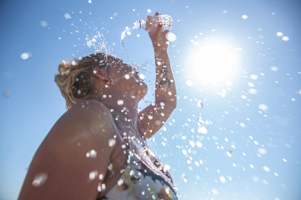 A young woman cools down under the sun with cold water during the summer heat. (Photo via Getty Images)