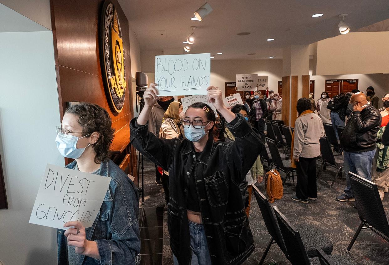 Students and community members hold signs as they march out of The Ohio State University Longaberger Alumni House on Thursday. The protesters called on university trustees to divest from corporations they say support Israeli and fossil fuel companies.