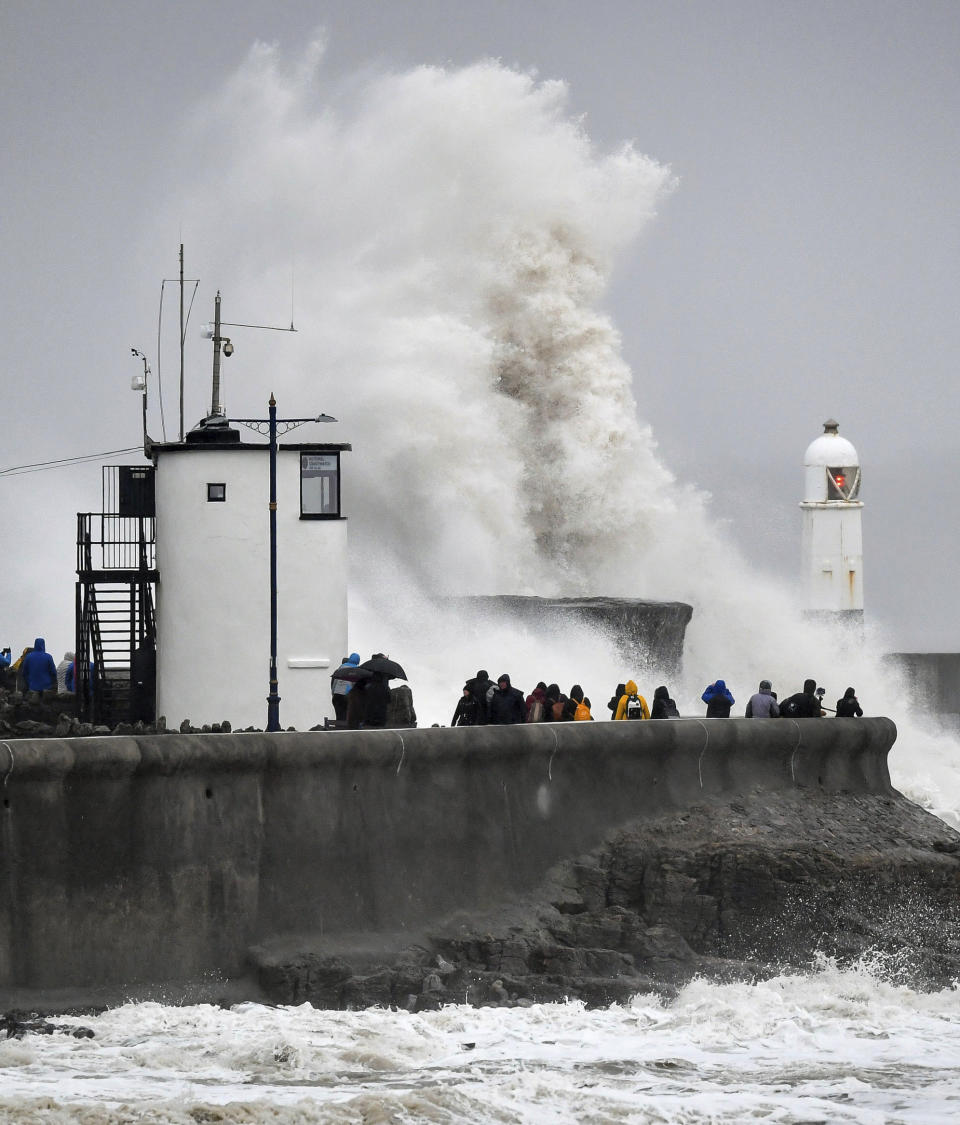 Gente contempla las olas y el mar agitado que se estrellan contra el muro del puerto de Porthcawl, Gales, cuando la tormenta Dennis atraviesa el país, sábado 15 de febrero de 2019. Gran Bretaña enfrenta un segundo fin de semana de tormentas invernales e inundaciones. (Ben Birchall/PA via AP)