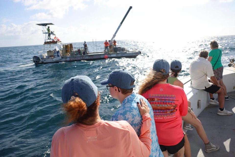 Debbie Pace puts a hand on the back of her son Aiden, 13, as the family watches a barge crew lower Jeffrey Pace’s reef ball into the water.