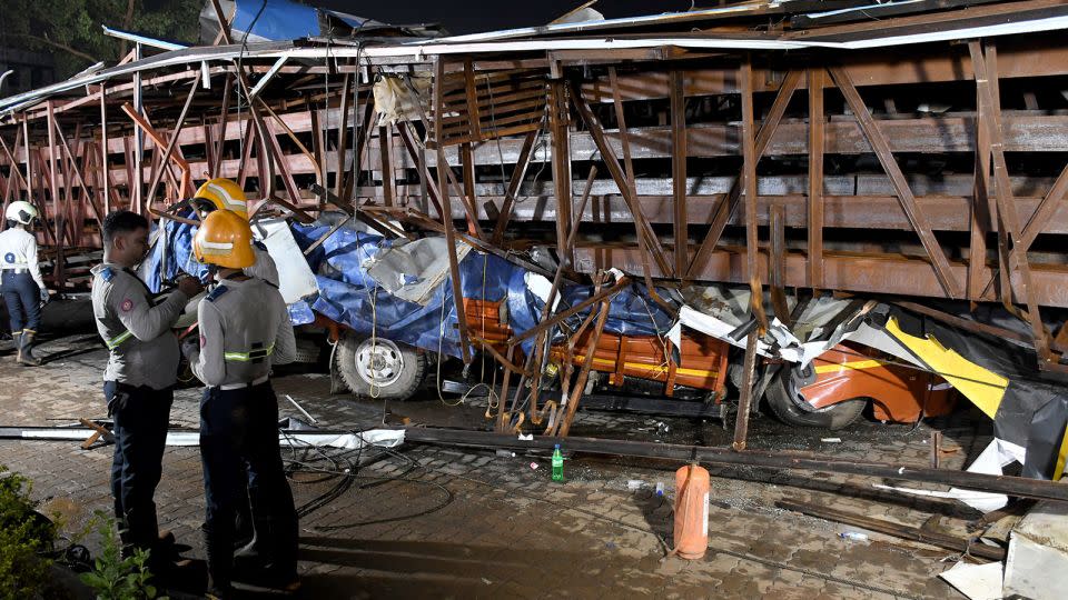 Firefighters stand next to vehicles crushed by the billboard, which fell during a rainstorm in Mumbai, India, on May 13, 2024. - Stringer/Reuters