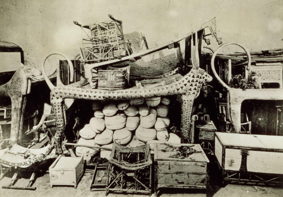 Photograph of a collection of items excavated from Tutankhamun's tomb, including furniture, chests, and various artifacts, arranged in a dense pile