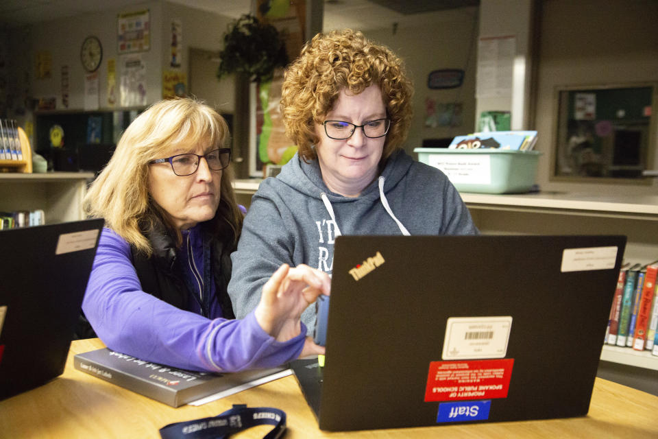 In a Sunday, March 15, 2020 photo, Jan McGowan, left, and Heather Miciak video chat with another teacher at Regal Elementary School as they create labels containing student login information for a digital program called Clever, which allows students access to educational resources, in Spokane, Wash. Many teachers and school employees used Sunday to gather materials for students to take home, amongst other preparations, as Spokane Public Schools close in an attempt to slow the spread of COVID-19 after Monday. (Libby Kamrowski/The Spokesman-Review via AP)