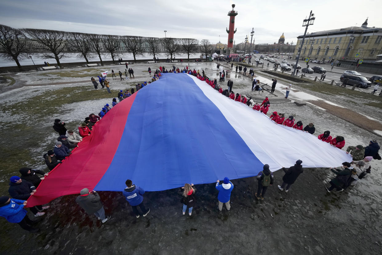 Young people unfurl a giant Russian flag during an action to mark the ninth anniversary of the Crimea annexation from Ukraine in St. Petersburg, Russia, Saturday, March 18, 2023. (AP Photo/Dmitri Lovetsky)