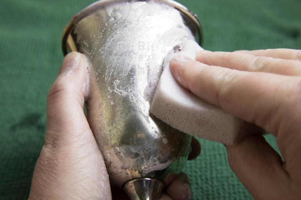 Person using a soapy sponge to clean a pewter goblet.