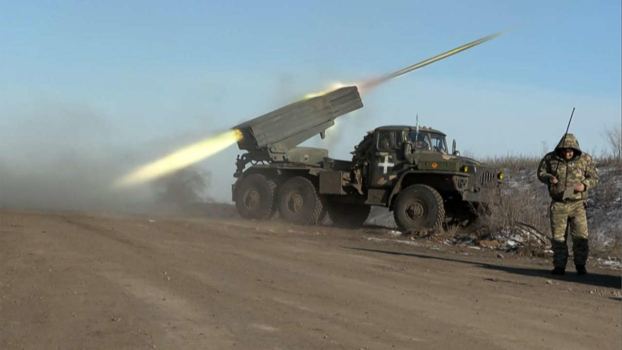 This grab taken from AFP video footage shows a member of Ukraine's military looking away as a BM-21'Grad' MLRS 122mm rocket launcher fires on the outskirts of Soledar on January 11, 2023. - Ukrainian President Volodymyr Zelensky has said fighting is still raging in a key eastern frontline city that a Russian mercenary group earlier said it controlled, as Moscow announced a new military commander in Ukraine. The fate of Soledar in eastern Ukraine was uncertain after Russian group Wagner claimed it controlled the gateway town -- but the Kremlin cautioned against declaring victory prematurely. (Photo by Arman SOLDIN / AFP)