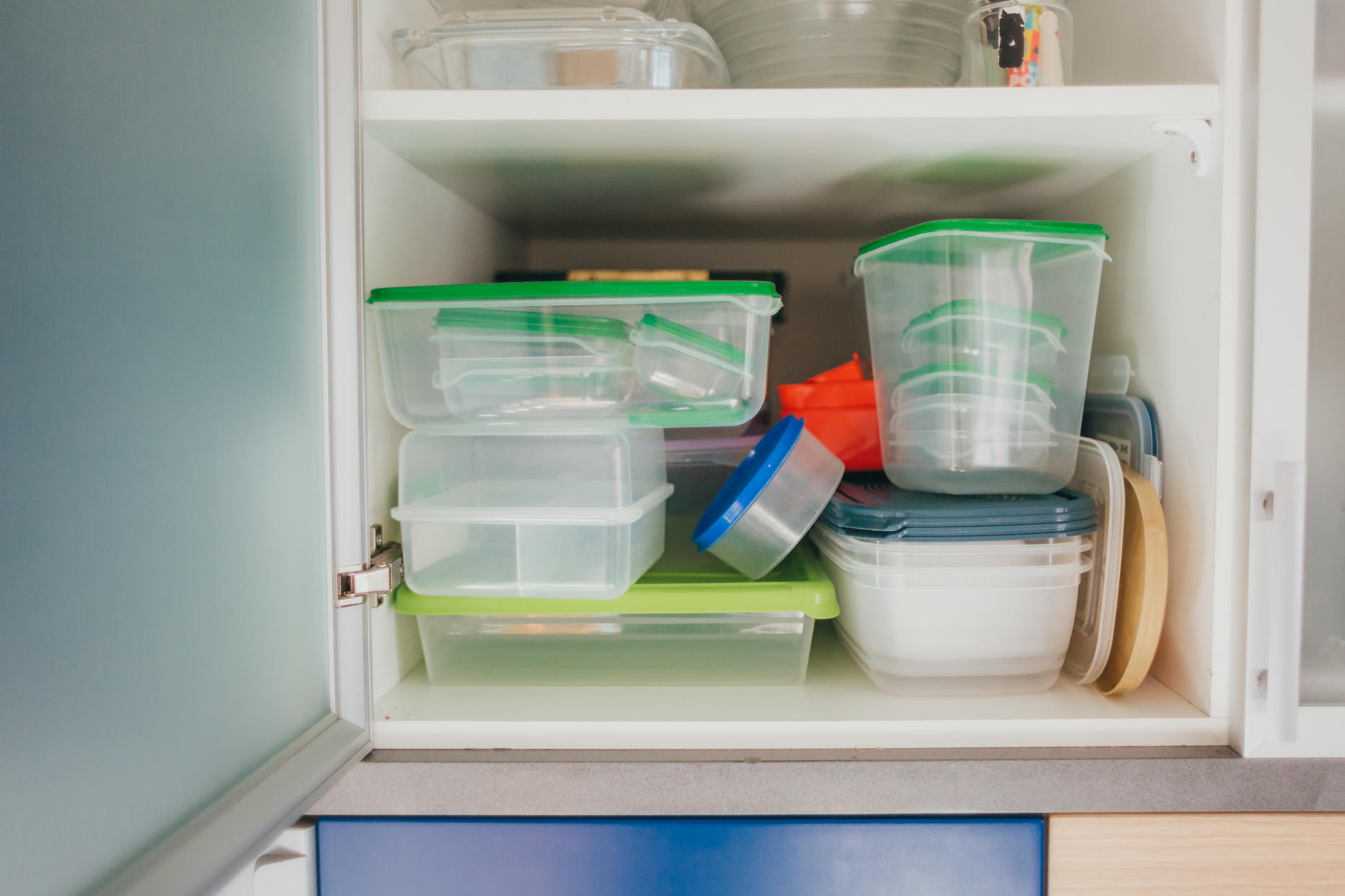 A messy kitchen cabinet that's full of plastic containers, illustrating a story on a messy kitchen and how to declutter it.