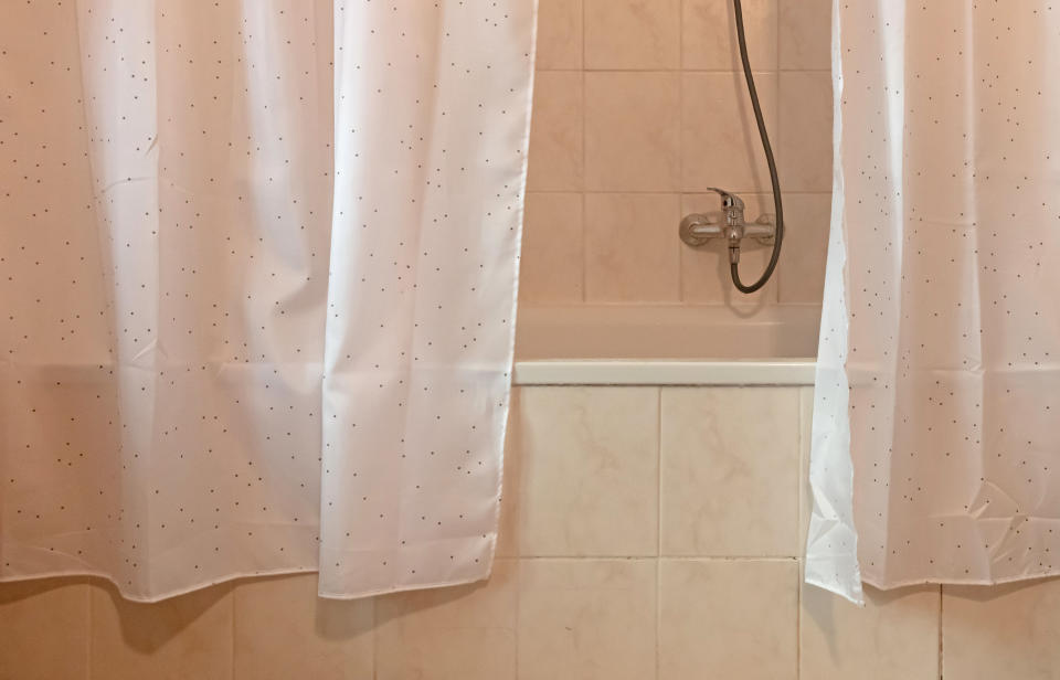 A white shower curtain hanging on the outside of a tub