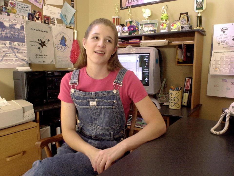 A girl in a pink shirt and overalls sits in front of her computer in 2000