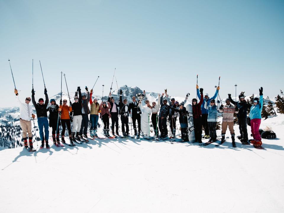 A group of people pose together holding skis on a snowy mountain.