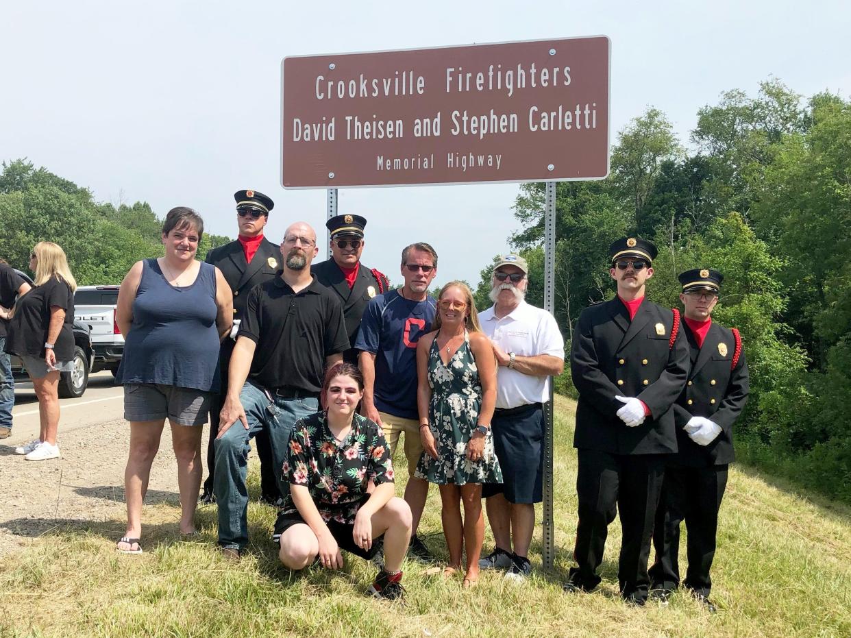 The families of fallen Crooksville firemen Steven Carletti and David Theisen stand under a road sign on Ohio 93 that was dedicated in their honor on Saturday by the state. Carletti and Theisen died fighting a house fire in the village on Feb. 5, 1998.