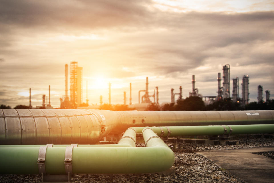 Pipelines heading into an industrial complex with the sun shining in the background.