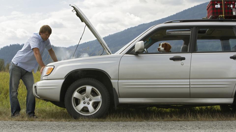 man checking engine of broken down car